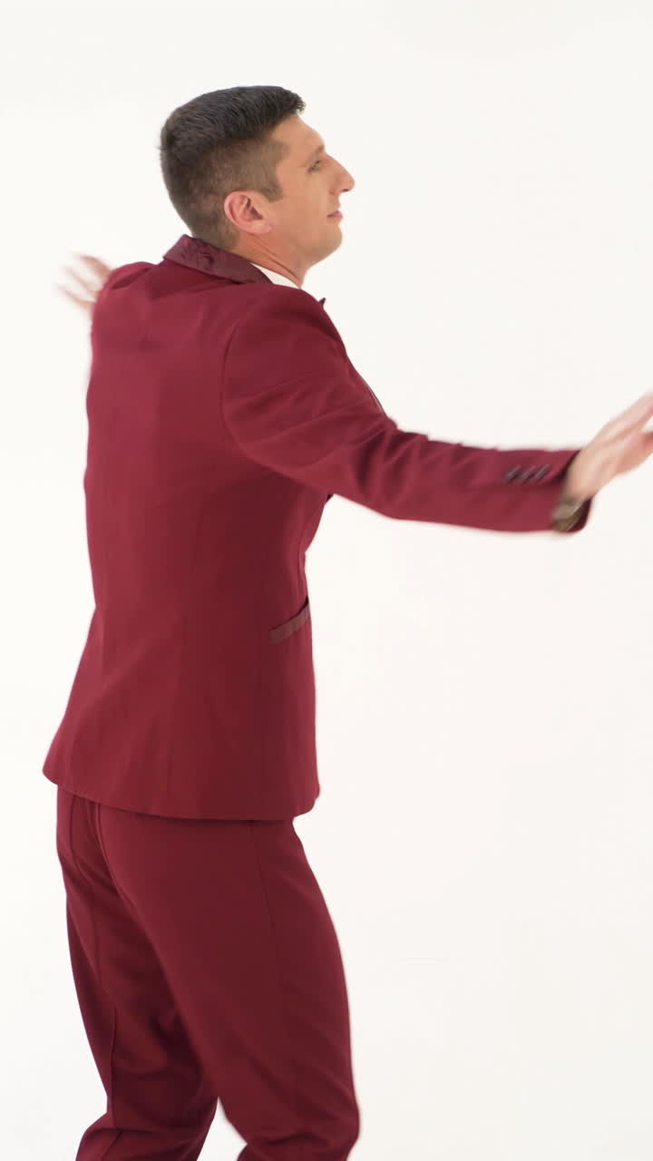 fun showman in red suit is waving his arms and spinning around himself on a white background in the studio Vertical video