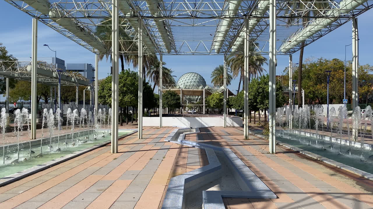 Fontane moderne e un pergolato in metallo incorniciano il parco fluviale dell'Expo a Siviglia, con l'ampio padiglione sferico sullo sfondo
