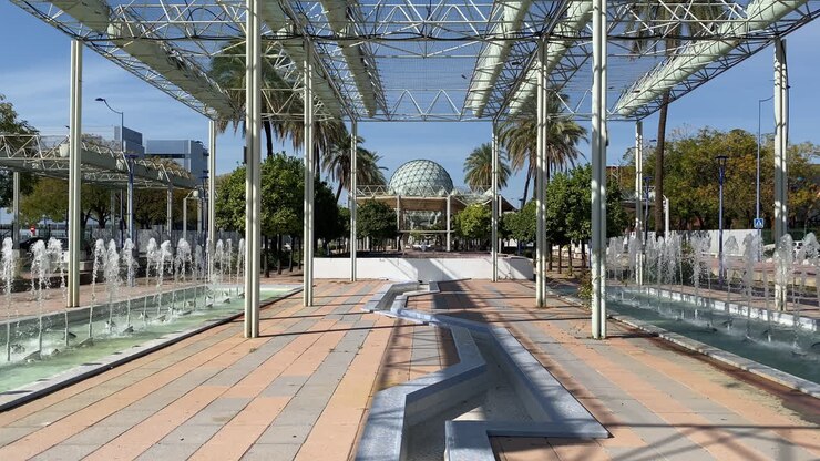 Fontane moderne e un pergolato in metallo incorniciano il parco fluviale dell'Expo a Siviglia, con l'ampio padiglione sferico sullo sfondo