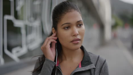 portrait-of-young-woman-puts-on-earphones-looking-at-camera-enjoying-listening-to-music-in-urban-city-street-real-people-series