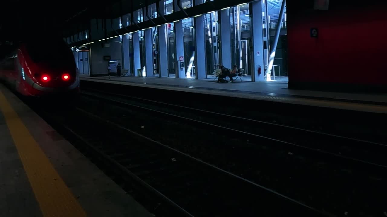 A sleek red train moves along a dimly lit station platform at night, showcasing modern rail design.