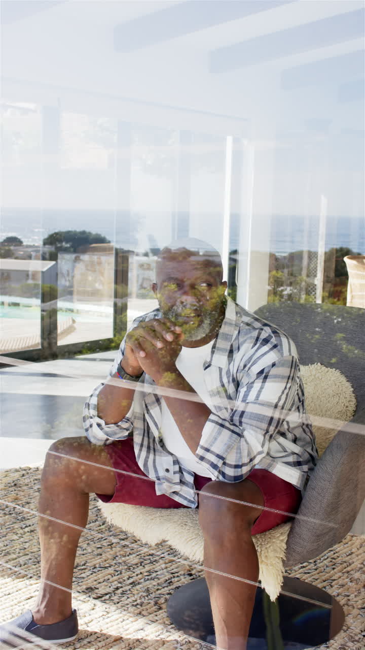 Vertical video: Reflecting through glass, mature man sitting indoors, contemplating view outside