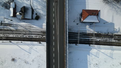 drone-top-down-railway-viaduct-in-winter-scenery,-black-asphalt-road-with-white-directional-arrows