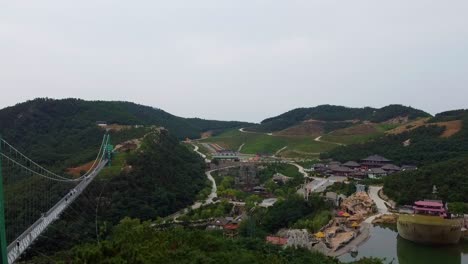 vista aérea ascendente detrás de los árboles que revela un puente de vidrio suspendido y un hermoso paisaje en el parque temático huaxiacheng en weihai, china