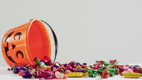 Scary-halloween-pumpkin-printed-bucket-full-of-candies-fallen-against-grey-background