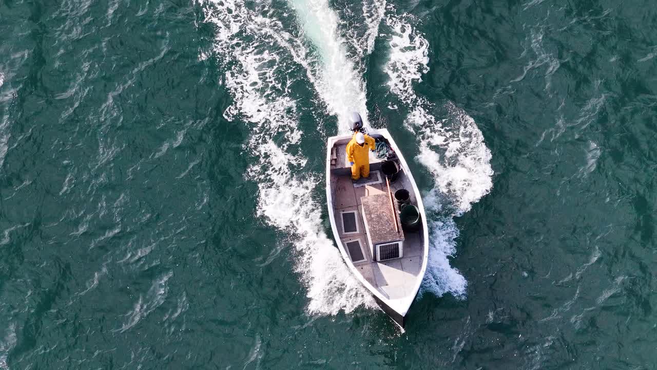 Aerial view of fishing boat with sailor moving through ocean waves, bright daylight, steady camera