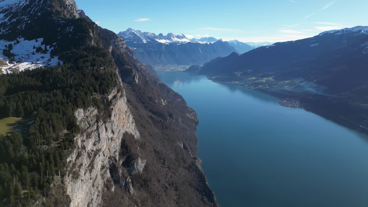 el dron se inclina hacia abajo a lo largo de escarpados acantilados de montaña y impresionante agua azul que refleja el cielo soleado en el lago walen, walensee, suiza