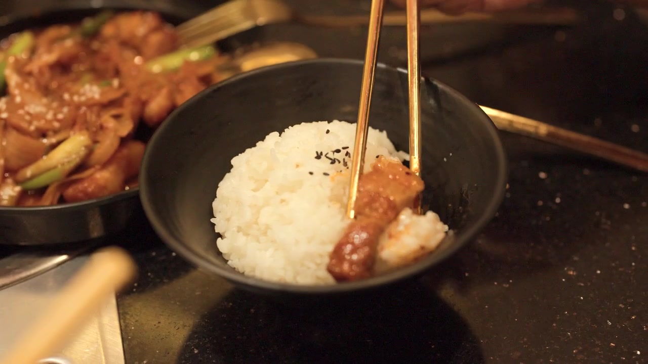 Close-up de hashis movendo carne de porco picante de uma frigideira para arroz branco cozido no vapor