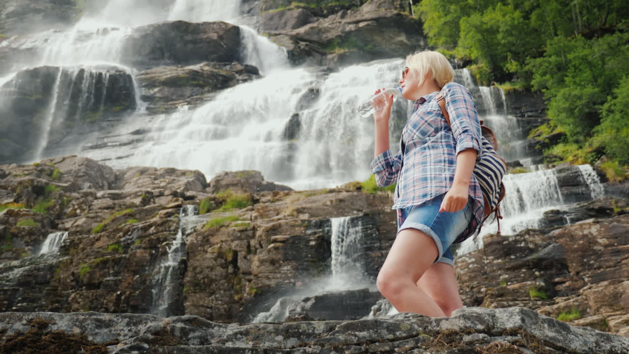 mujer joven bebe agua en el fondo de la cascada gemela tvindefossen en noruega bebida limpia