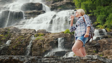 Junge-Frau-Trinkt-Wasser-Auf-Dem-Hintergrund-Des-Zwillingswasserfalls-Tvindefossen-In-Norwegen-Sauberes-Getränk