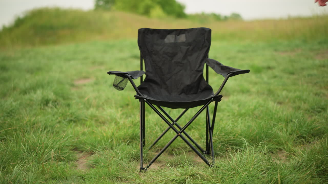 A woman in a white dress reaches out to a black portable chair set on lush green grass, creating a serene outdoor scene