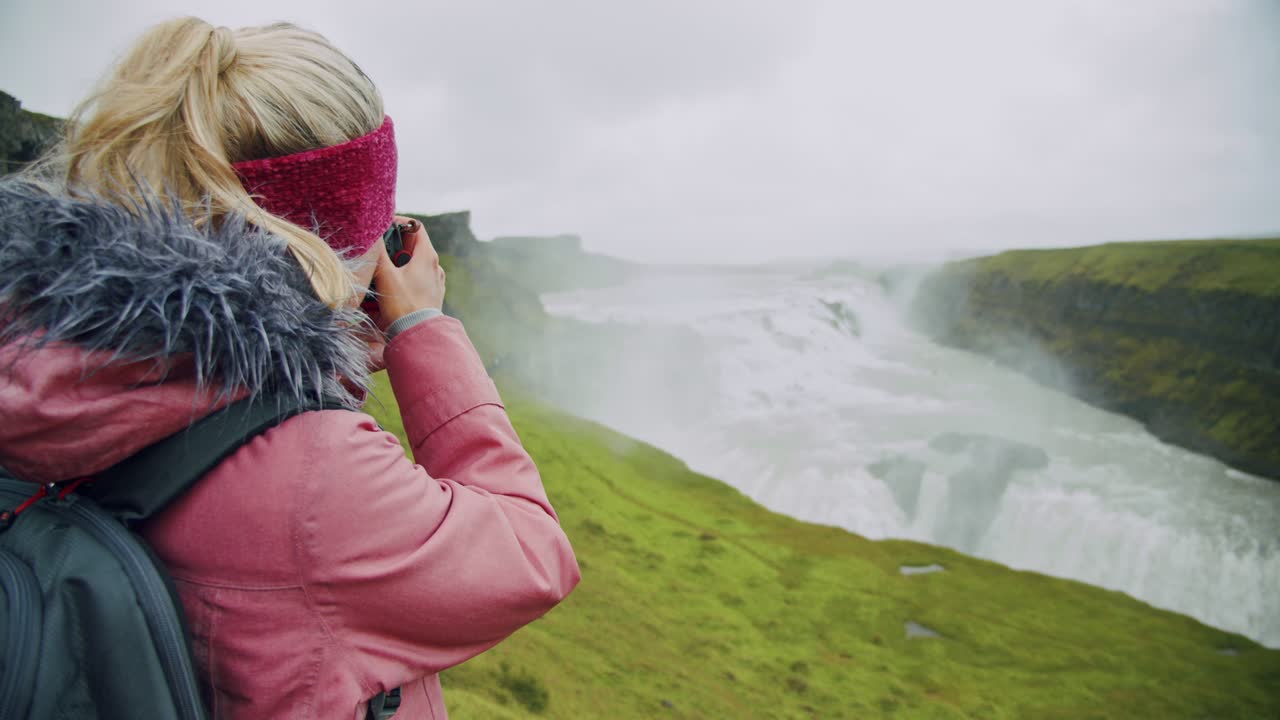 primer plano de una mujer adulta tomando una fotografía en la cascada de gullfoss, la famosa atracción y destino histórico de islandia en el círculo dorado.