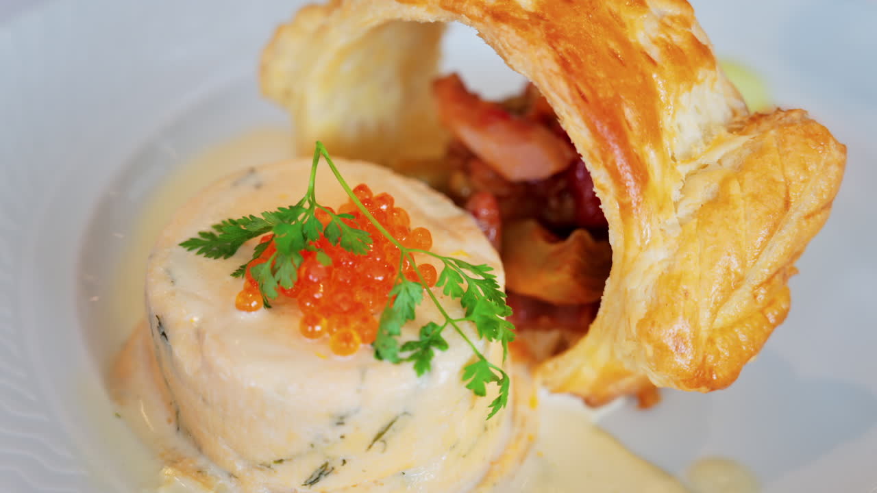 Close up of a fish mousse with salmon roe and puff pastry on a white plate at a restaurant