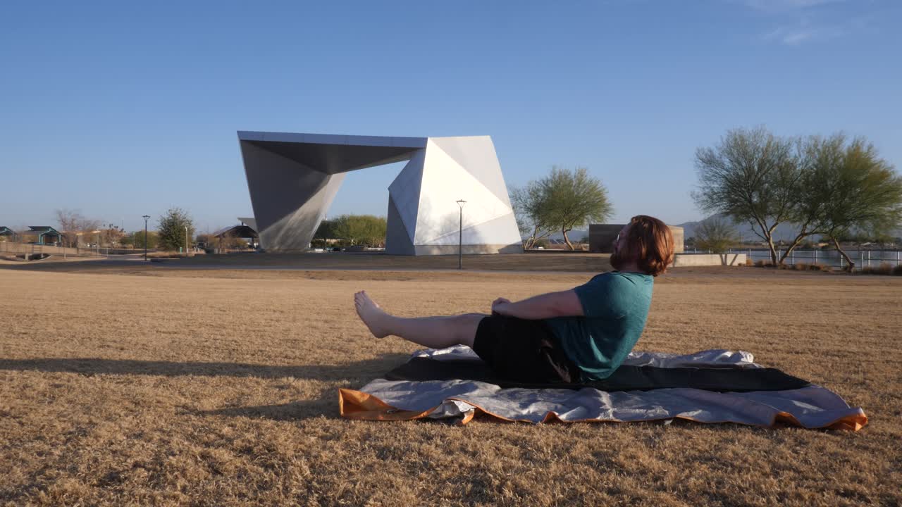 Red hair male doing leg raises in a Gilbert Arizona park with an amphitheater behind them.