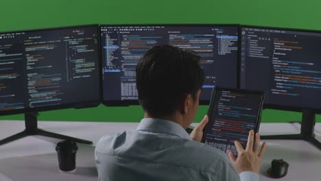 back view of asian man developer working with tablet while write code with multiple computer screens in green screen studio