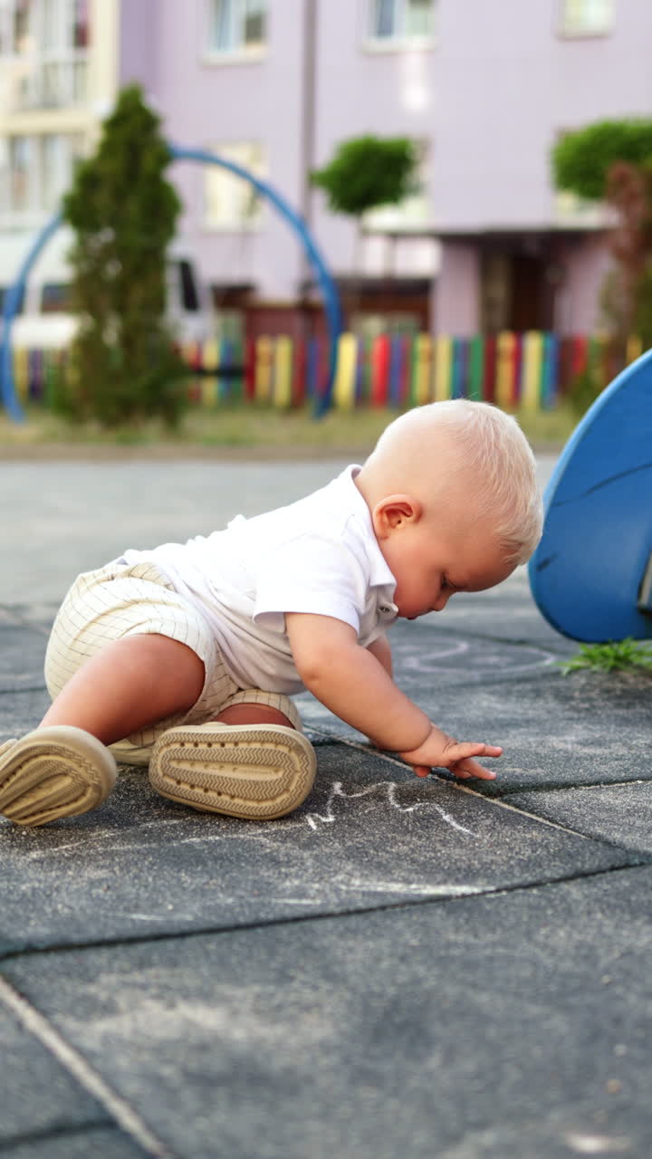 Un bambino disegna con il gesso sull'asfalto durante una passeggiata. Un bambino disegna con il gesso. Abbigliamento estivo per bambini.