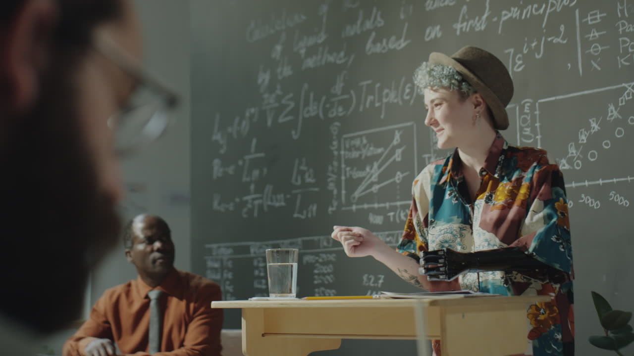 A speaker with a prosthetic arm delivers a lecture in a classroom setting with mathematical equations on the blackboard
