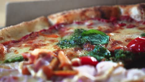 Closeup-shot-of-tasty-Italian-pizza-with-pesto-sauce-in-a-cardboard-pizza-box-on-the-table,-rotating-shot