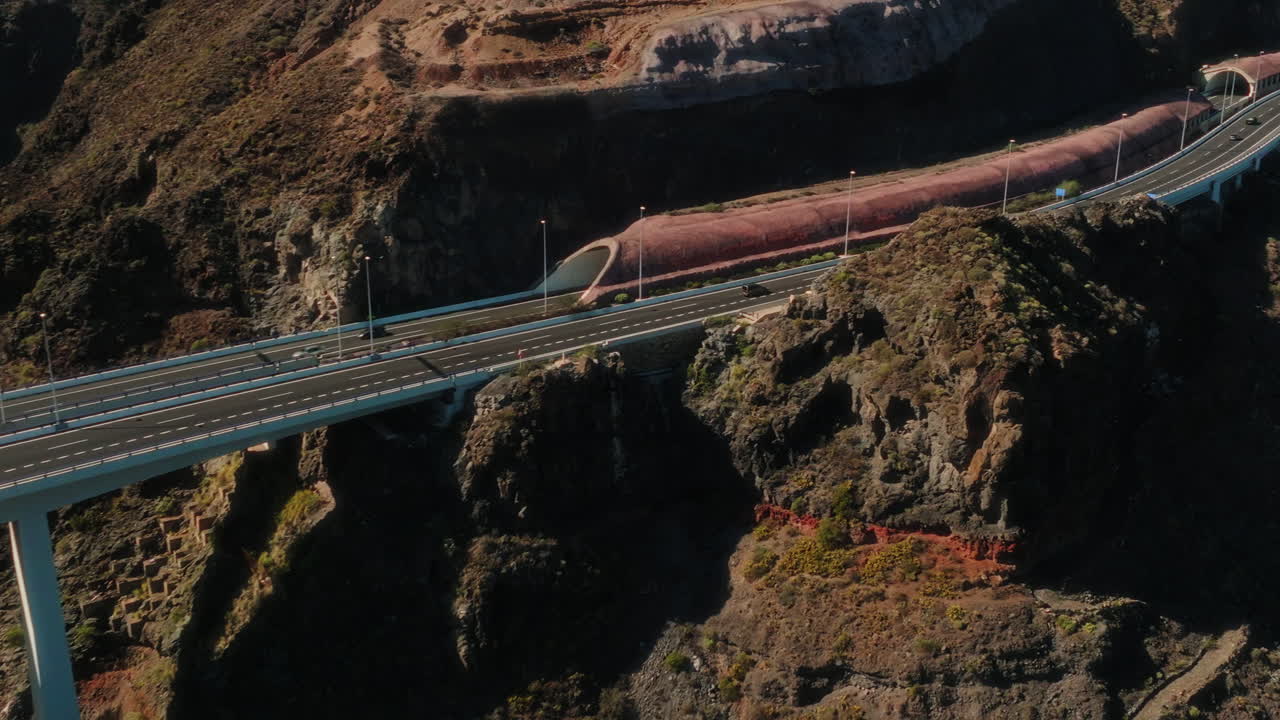 Aerial: white bridge in a valley with traffic and cars during the day in Gran Canaria, Spain, pan drone shot