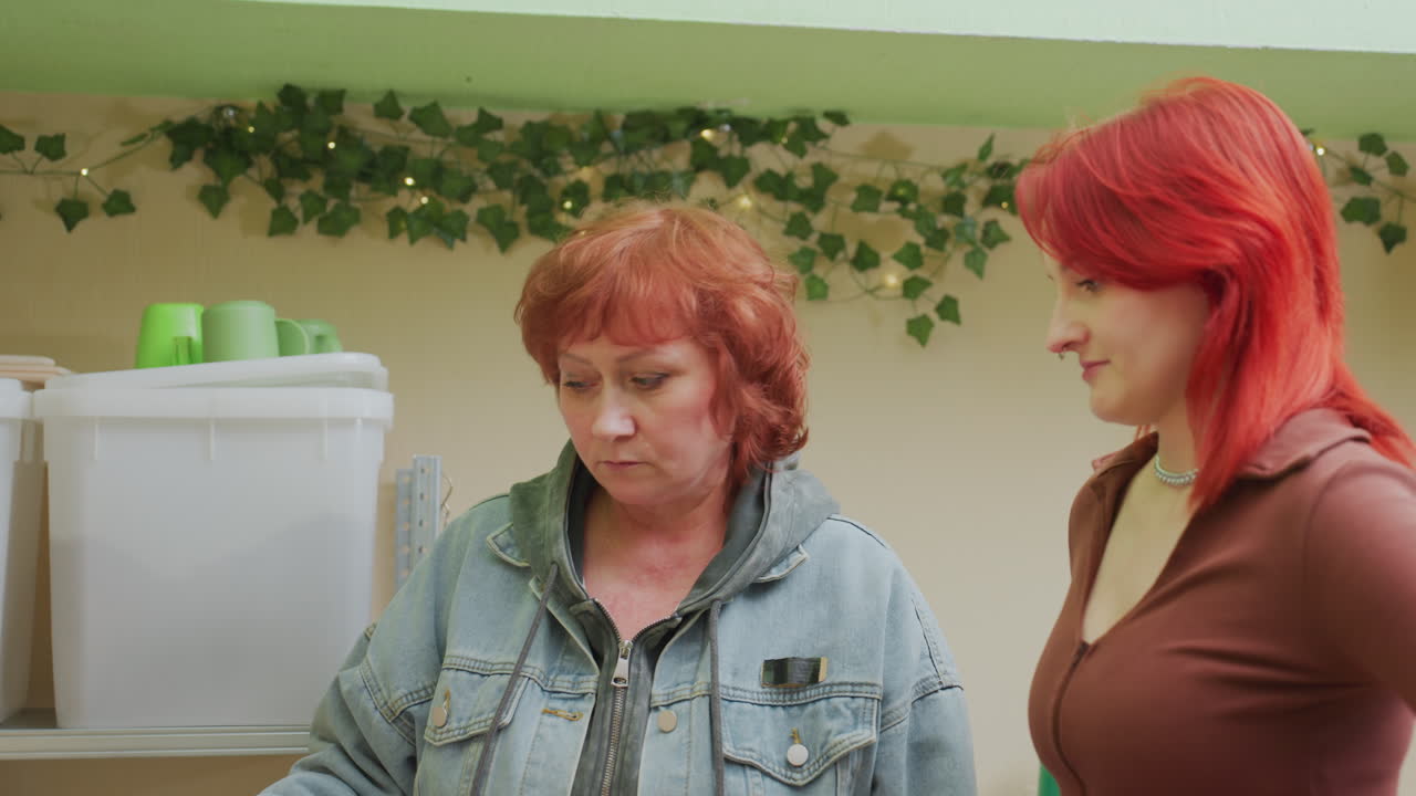 caucasian women at pantry share moment as older coordinator reviews inventory while younger shopper holds bananas subtle eye contact and reassurance, gentle conversation about needs, compassionate