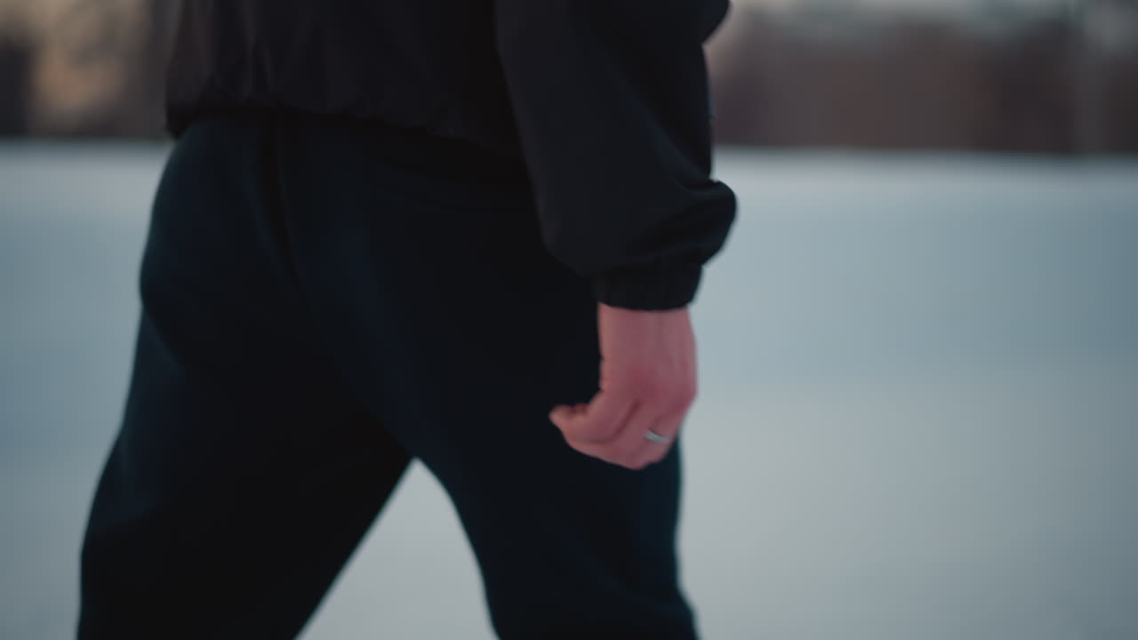 close up of individual in black jogger and patterned winter jacket gliding on smooth ice surface wearing ring on finger, with blurred skaters and residential buildings in background