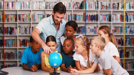 School-kids-and-teacher-looking-at-globe-in-library