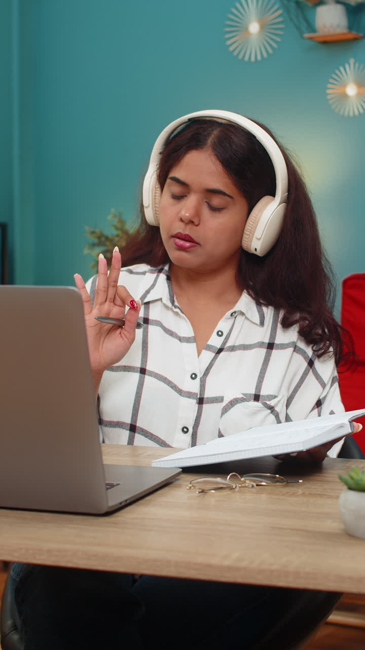 Indian woman nods in online lecture wearing headphones writing notes focused remote learning session