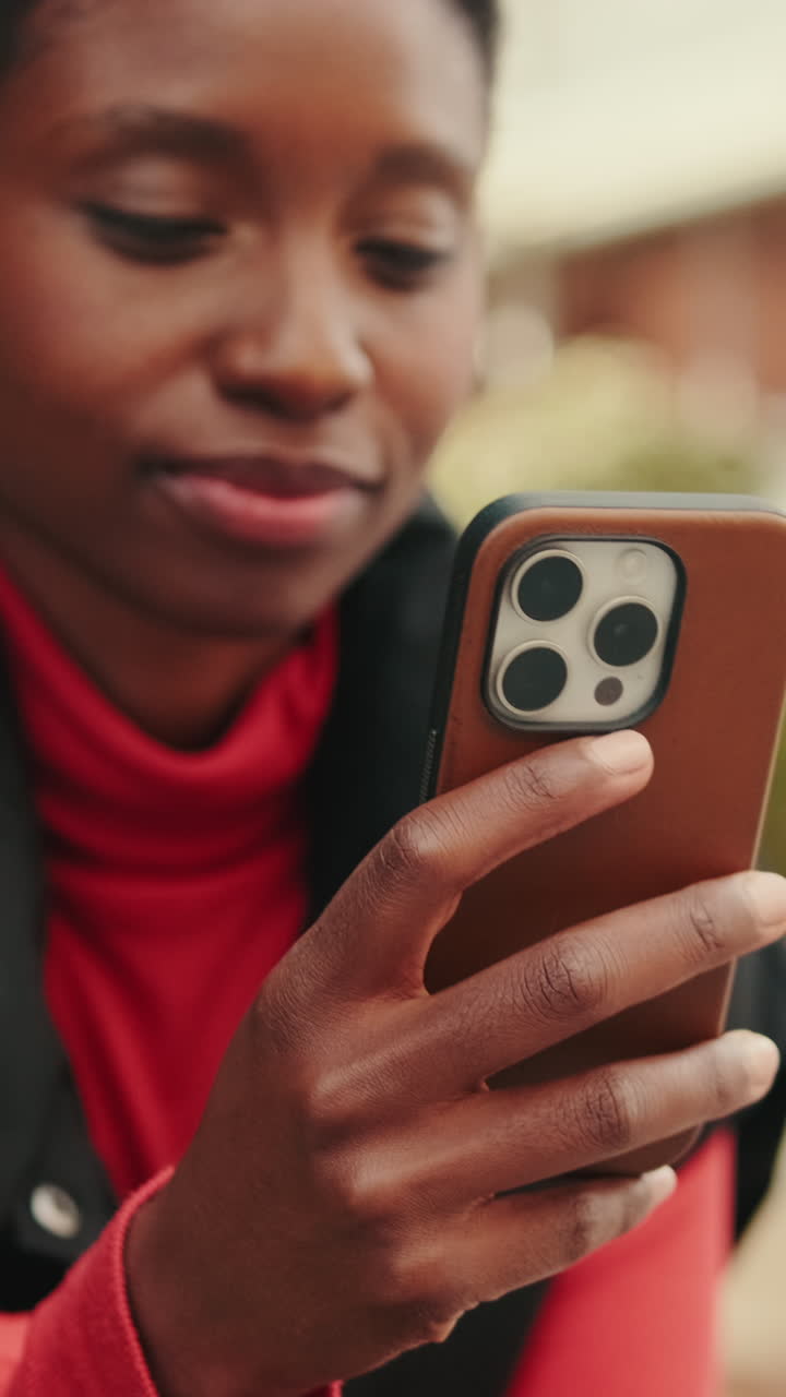Giovane donna di colore che sorride mentre usa lo smartphone all'aperto.