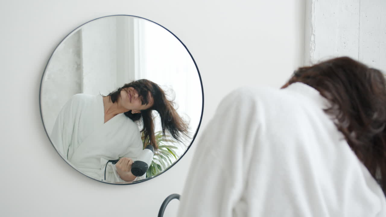 mujer secándose el cabello frente a un espejo