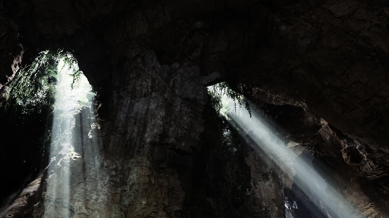 Light beams stream through openings in a cave surrounded by rugged rock