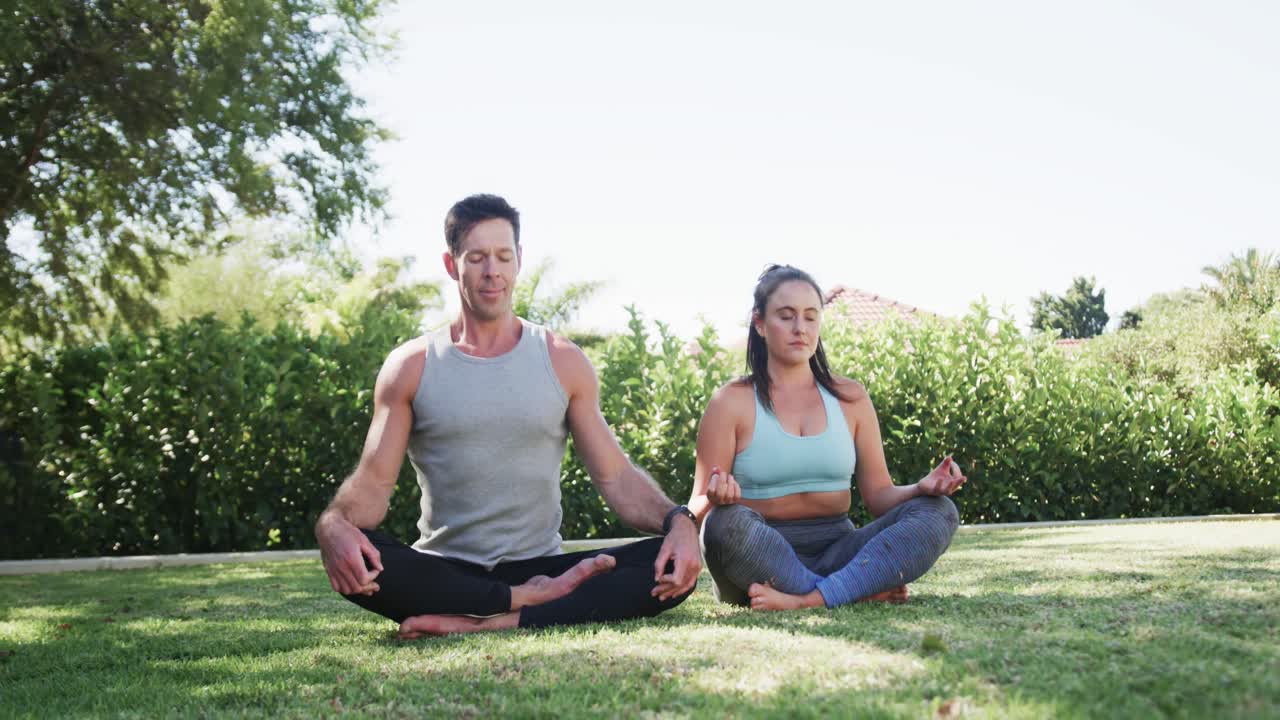 feliz pareja caucásica practicando meditación de yoga en un jardín soleado, cámara lenta
