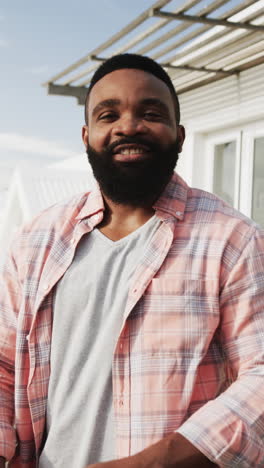vertical video of portrait of happy african american man on sunny terrace, slow motion