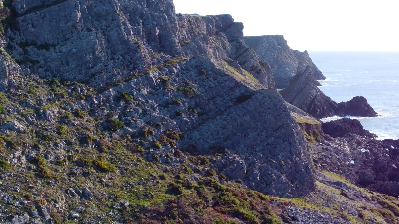 Parallax laterale aerea di un incredibile paesaggio marino con ripide montagne spettacolari. Clip di viaggio naturalistico con drone. Splendida costa gallese della penisola di Gower. Scatto iniziale di presentazione.