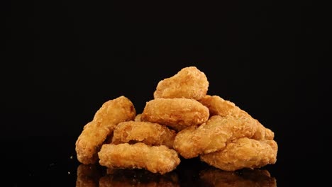 a stack of golden, breaded chicken nuggets spins smoothly on a glossy black surface under bright studio lighting, highlighting texture and appetizing color