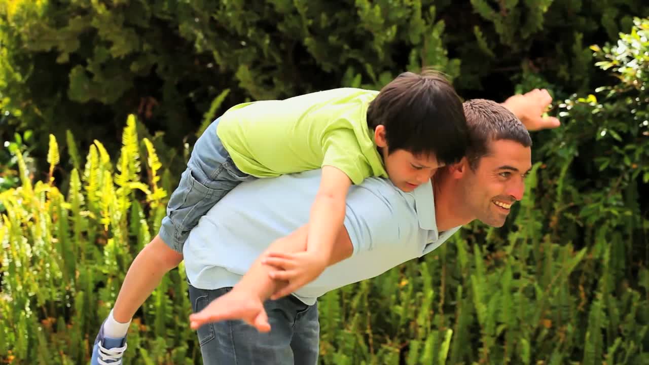 padre con su hijo en la espalda jugando en el jardín
