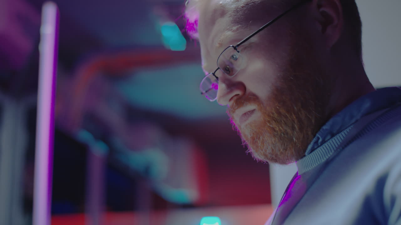 Primo piano di un uomo con occhiali e barba in un ambiente illuminato al neon