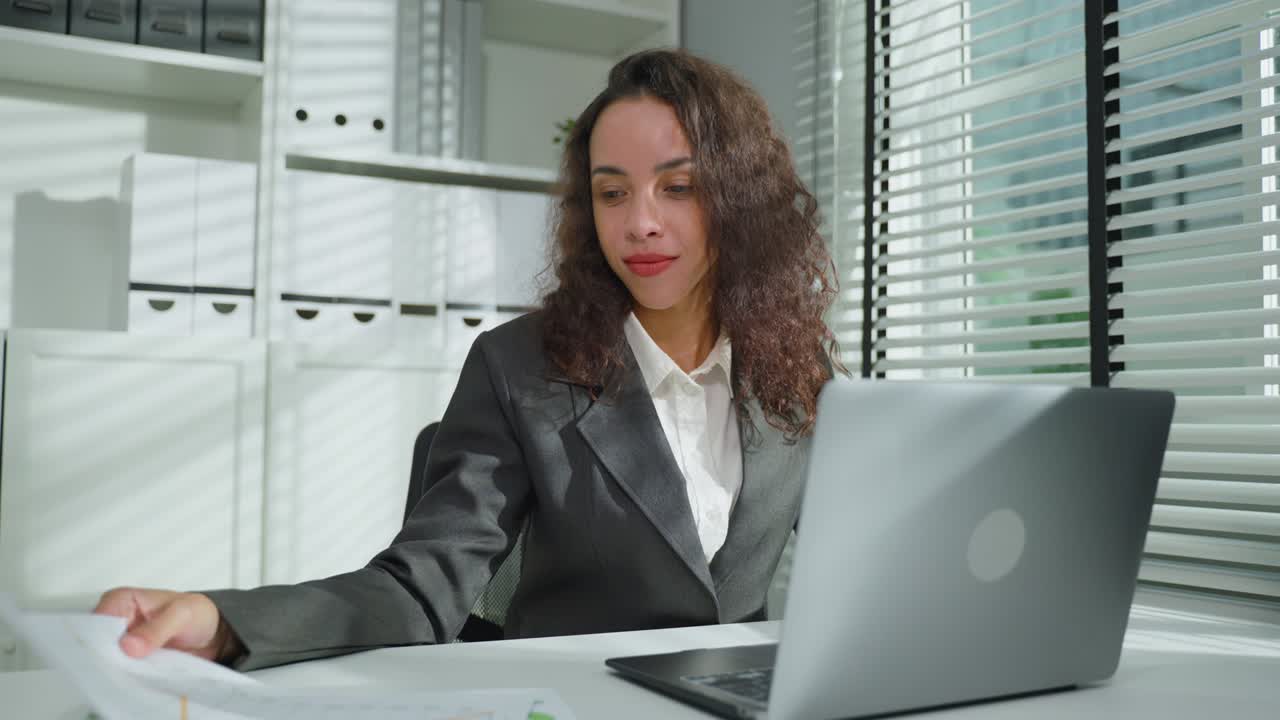 una mujer de negocios latina atractiva que trabaja demasiado tarde en la oficina por la noche. una joven y hermosa empleada profesional en ropa formal se sienta en la mesa en el lugar de trabajo, usa una computadora portátil y escribe en el teclado.