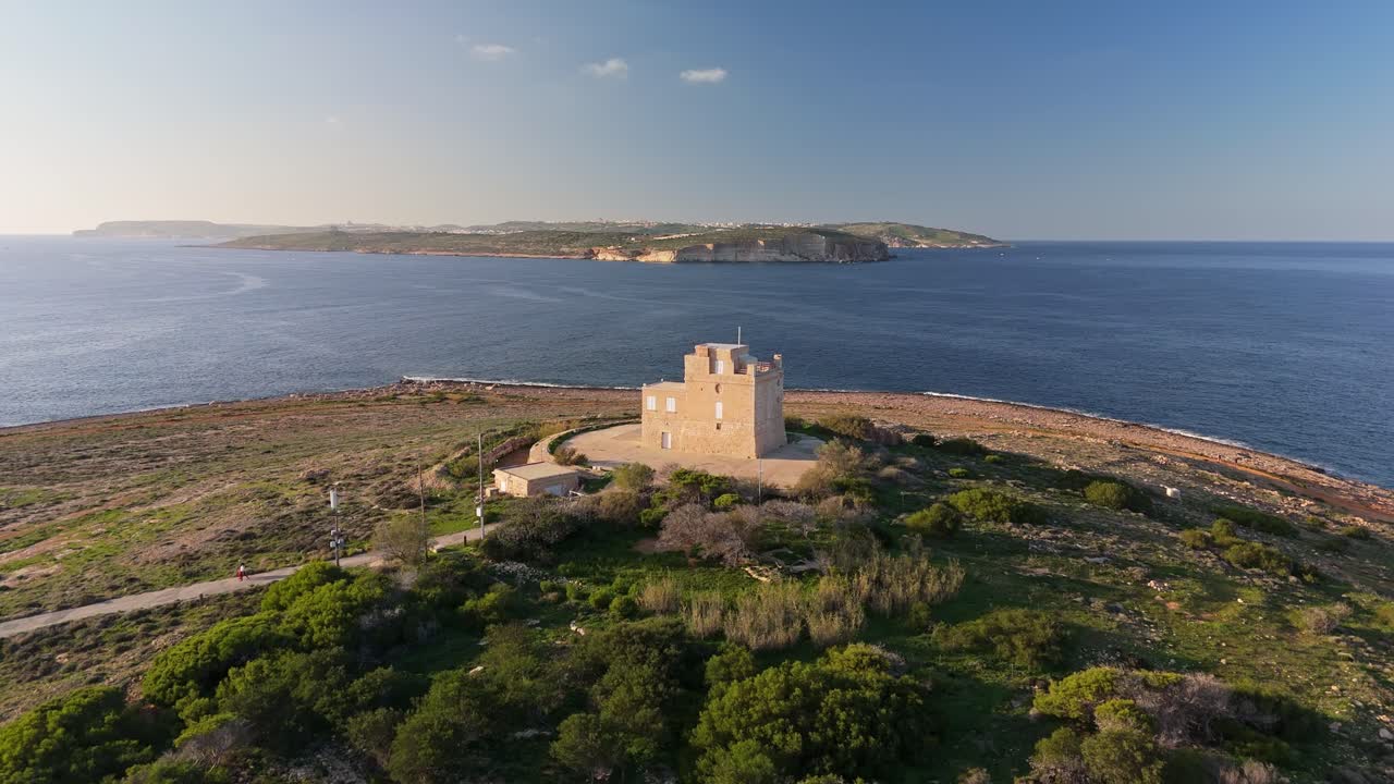 Veduta aerea della Torre Bianca restaurata a Mellieħa, Malta, che mette in mostra la sua architettura medievale tra paesaggi mediterranei, mare turchese e costa panoramica sotto un cielo soleggiato.