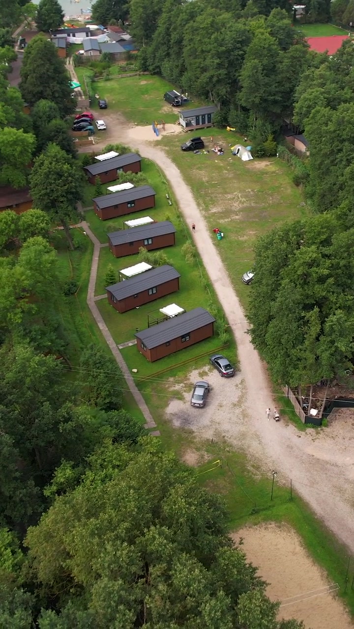 Filmisk luftfoto af et fredfyldt feriested med rækker af træferiehuse omgivet af frodig grøn skov i Kaszuby, Polen