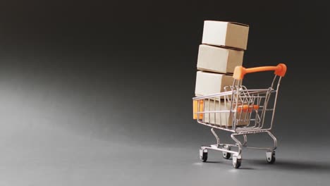 Shopping-trolley-with-stack-of-cardboard-boxes,-on-seamless,-lit-black-background-with-copy-space