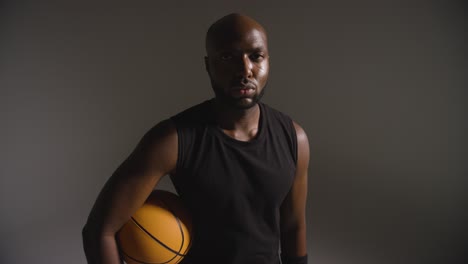 retrato de estudio de un jugador de baloncesto que sostiene la pelota bajo el brazo contra un fondo oscuro 3