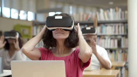 mujer madura sonriente configurando auriculares vr en la biblioteca
