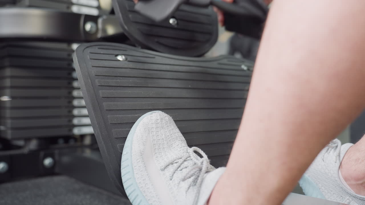 Male feet on pedal of weight machine stabilizing posture while hand reaches to grip handle before pull exercise in busy modern gym filled with equipment, focused form and fitness enthusiasts