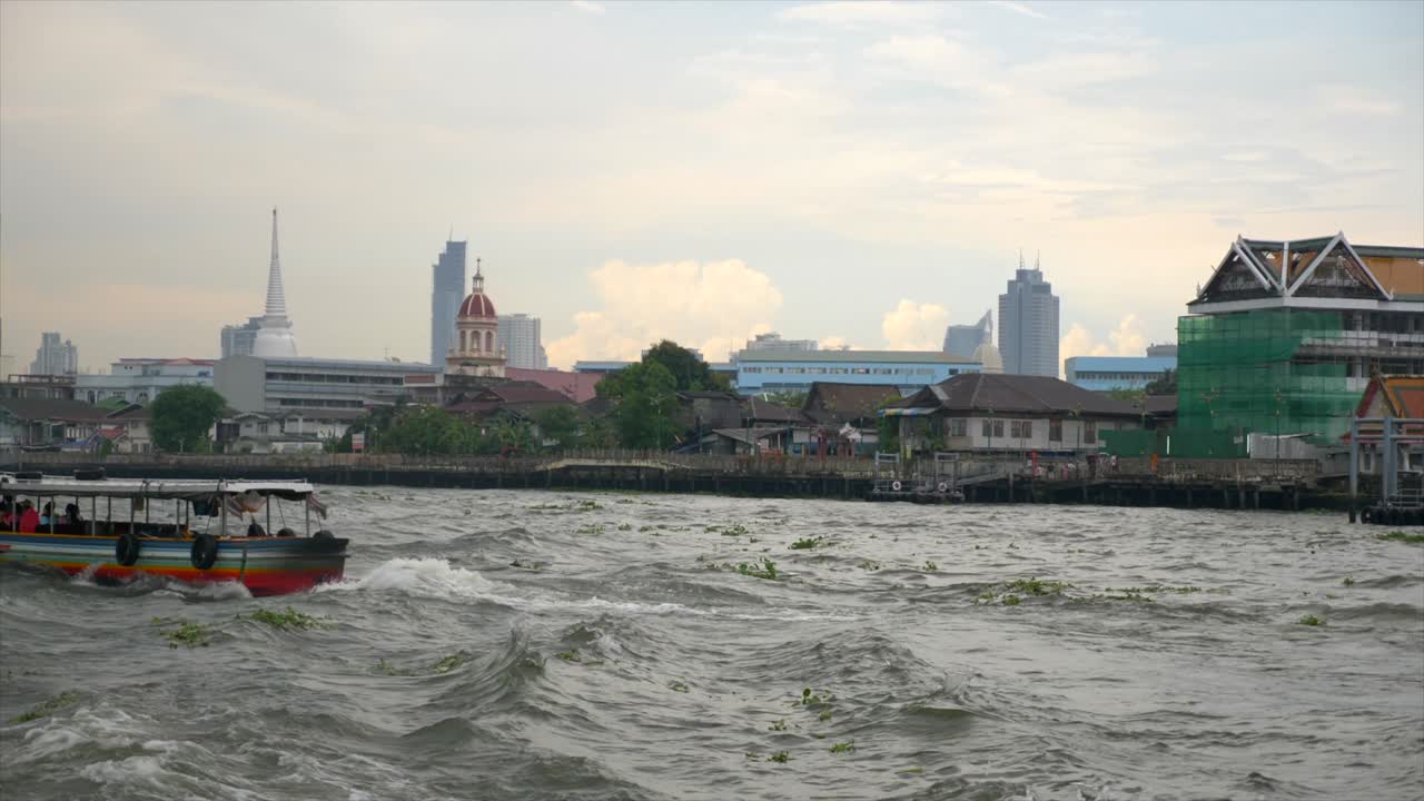shot of two transportation boats crossing the Chao Phraya river in Bangkok. The shot is taken from the water. On the background the traditional and modern buildings of the city.