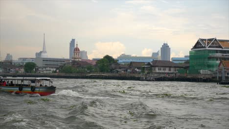shot of two transportation boats crossing the chao phraya river in bangkok. the shot is taken from the water. on the background the traditional and modern buildings of the city.