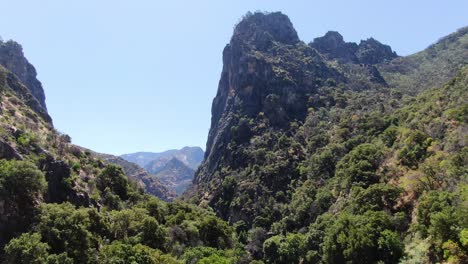 Aerial-back-to-front-shot-of-Sierra-NEvada-mountain-at-Kings-Canyon's-National-Park,-surrounded-by-vegetation,-bathed-in-California's-brilliant-sunlight