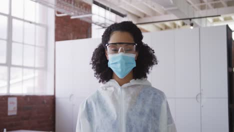 Portrait-of-mixed-race-female-cleaner-wearing-protective-face-mask-and-overalls