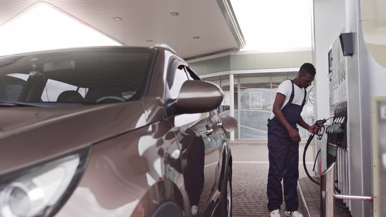 Ung, flot, afrikansk mandlig medarbejder på tankstation, der påfylder benzin på kundernes bil oversættelse