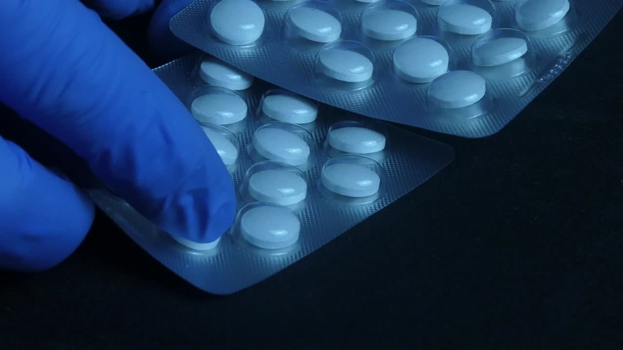 Close up of a medical professional in blue gloves holding two blister packs with white tablets