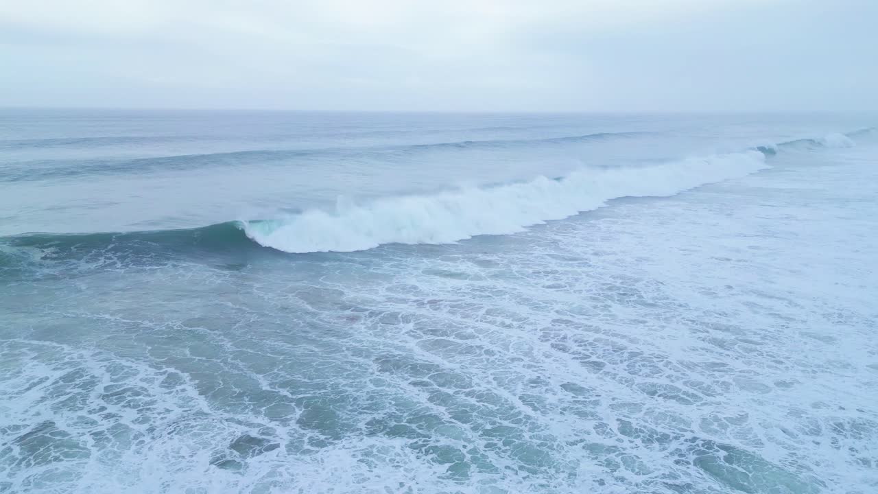Powerful ocean wave crashes near Aljezur coast under a soft blue morning sky